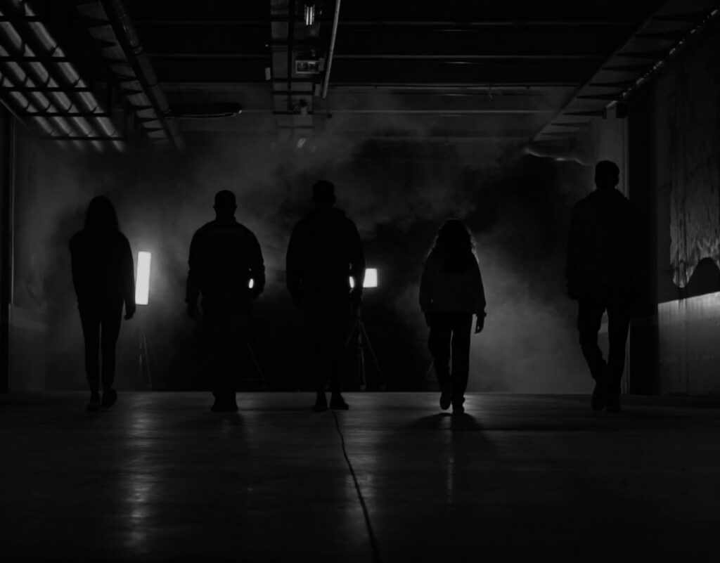 Cinq silhouettes à contre-jour dans un hangar sombre : l’équipe International ICS, visages non visibles